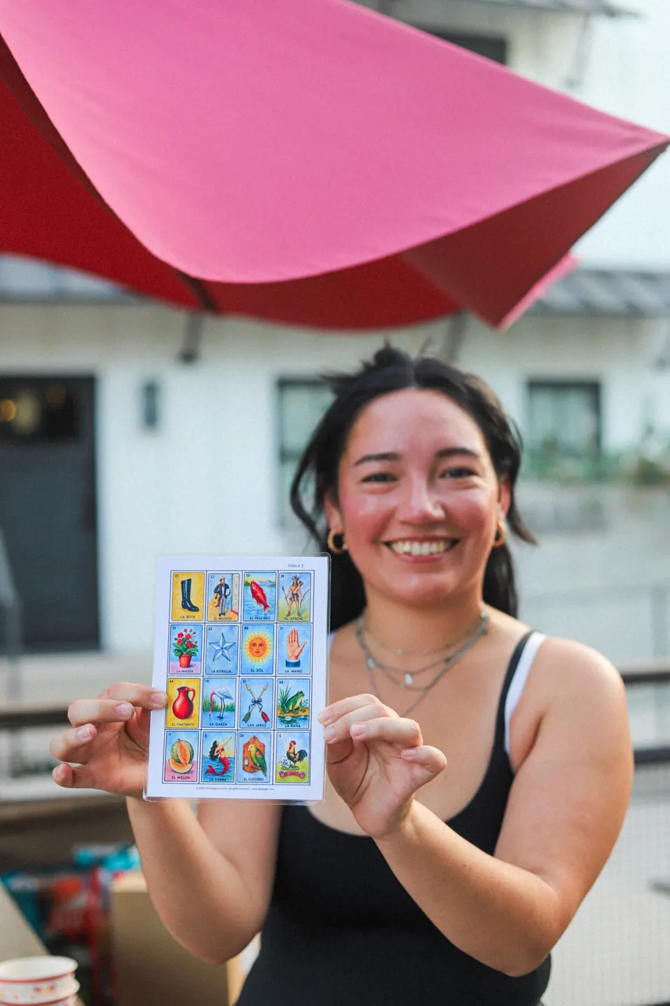 A smiling guest holding a lotería card at a community gathering
