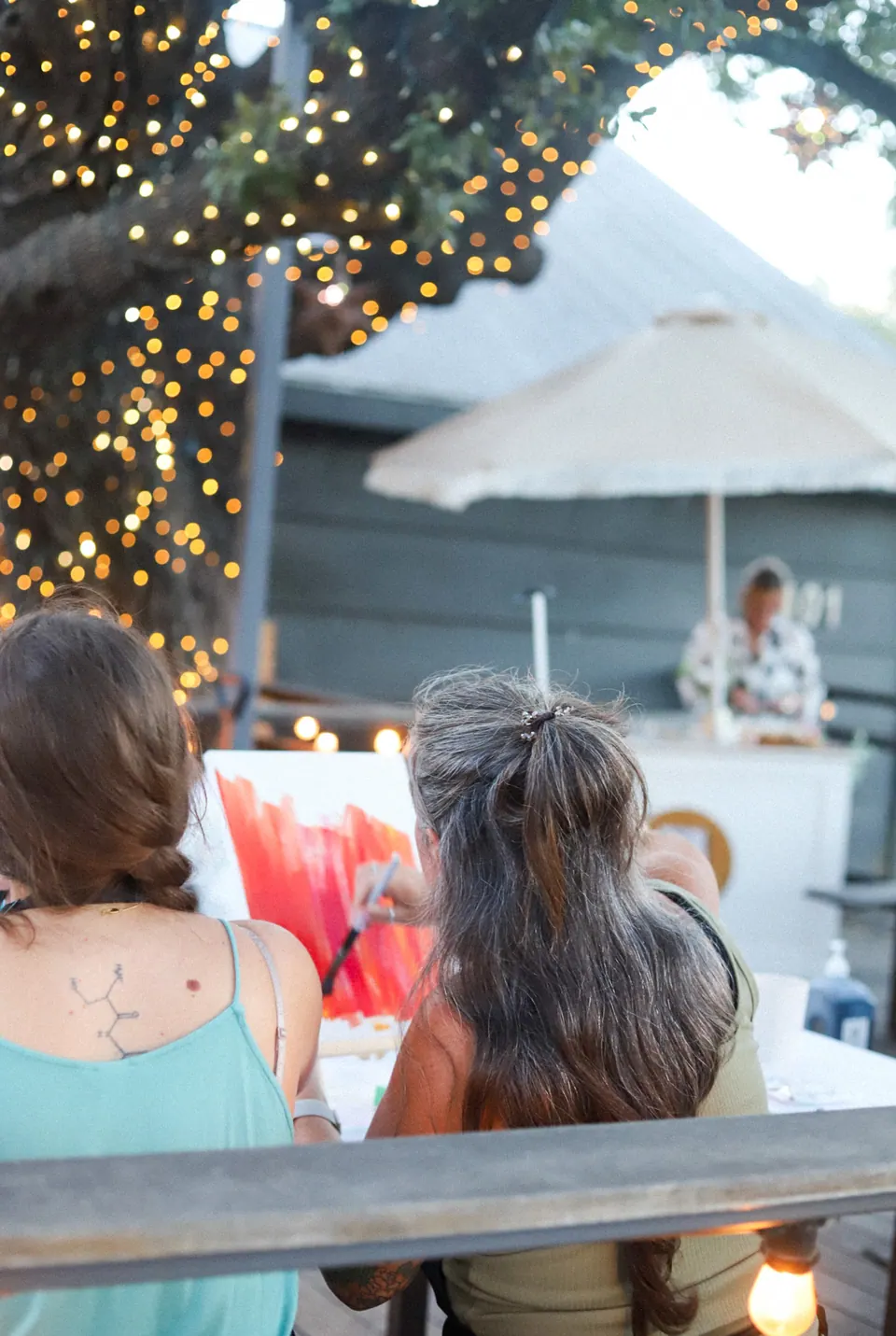 Guests painting together beneath a tree hung with warm lights
